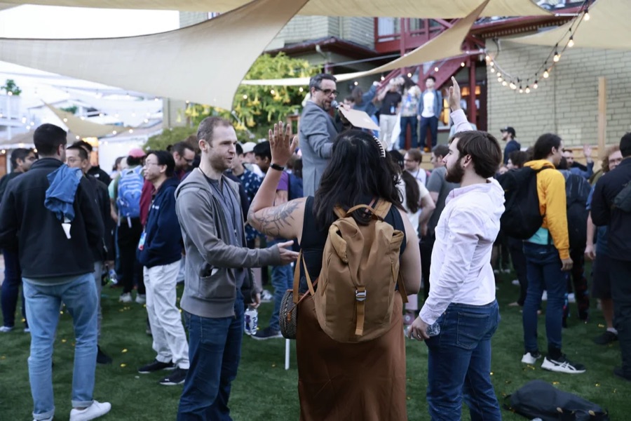 An outdoor facilitated session at a conference: a large crowd standing and talking in small groups.