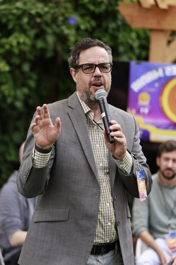 Misha Glouberman speaking into a microphone at a conference.