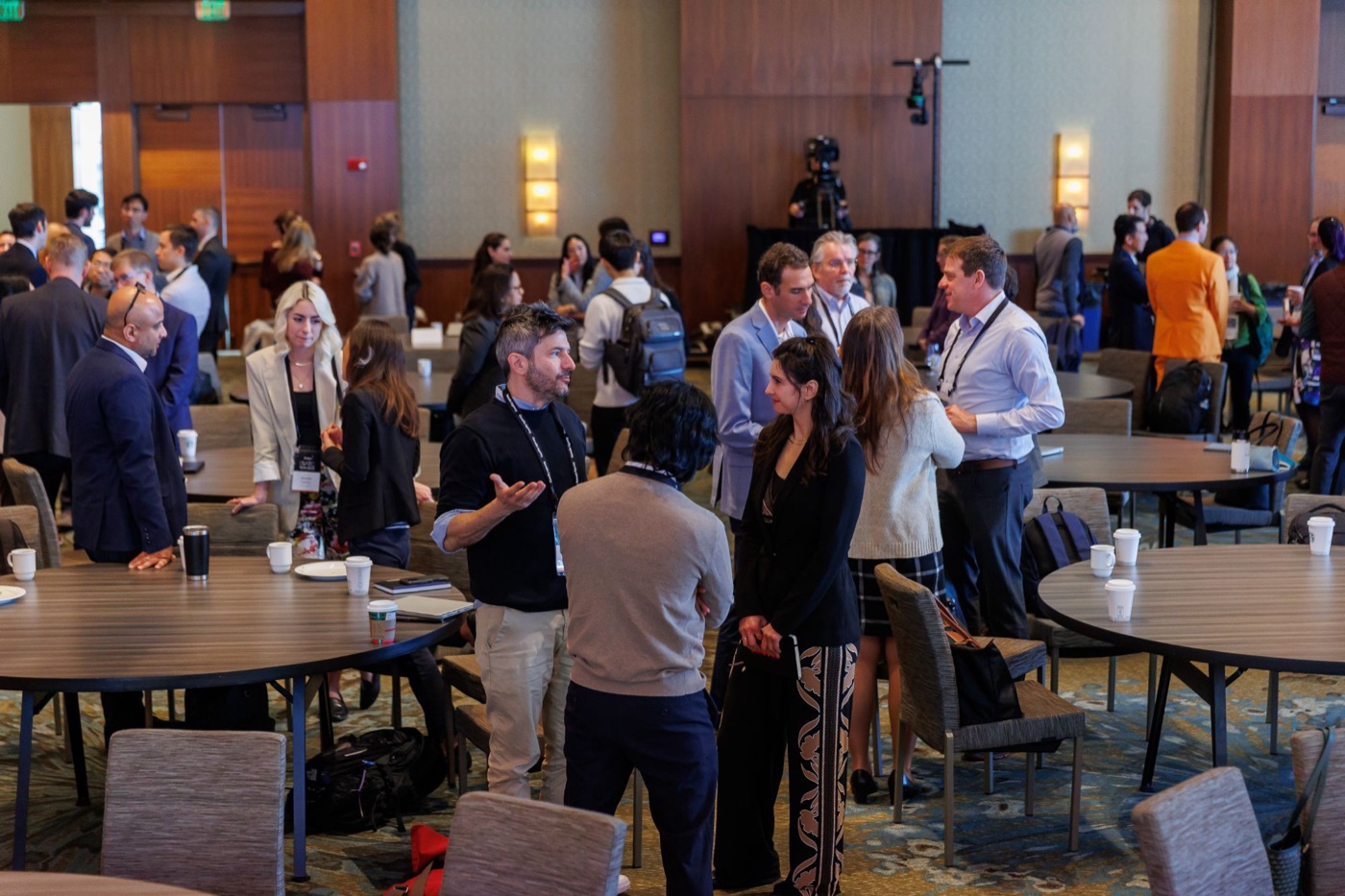 A ballroom full of conference attendees standing between round tables, talking in small groups.